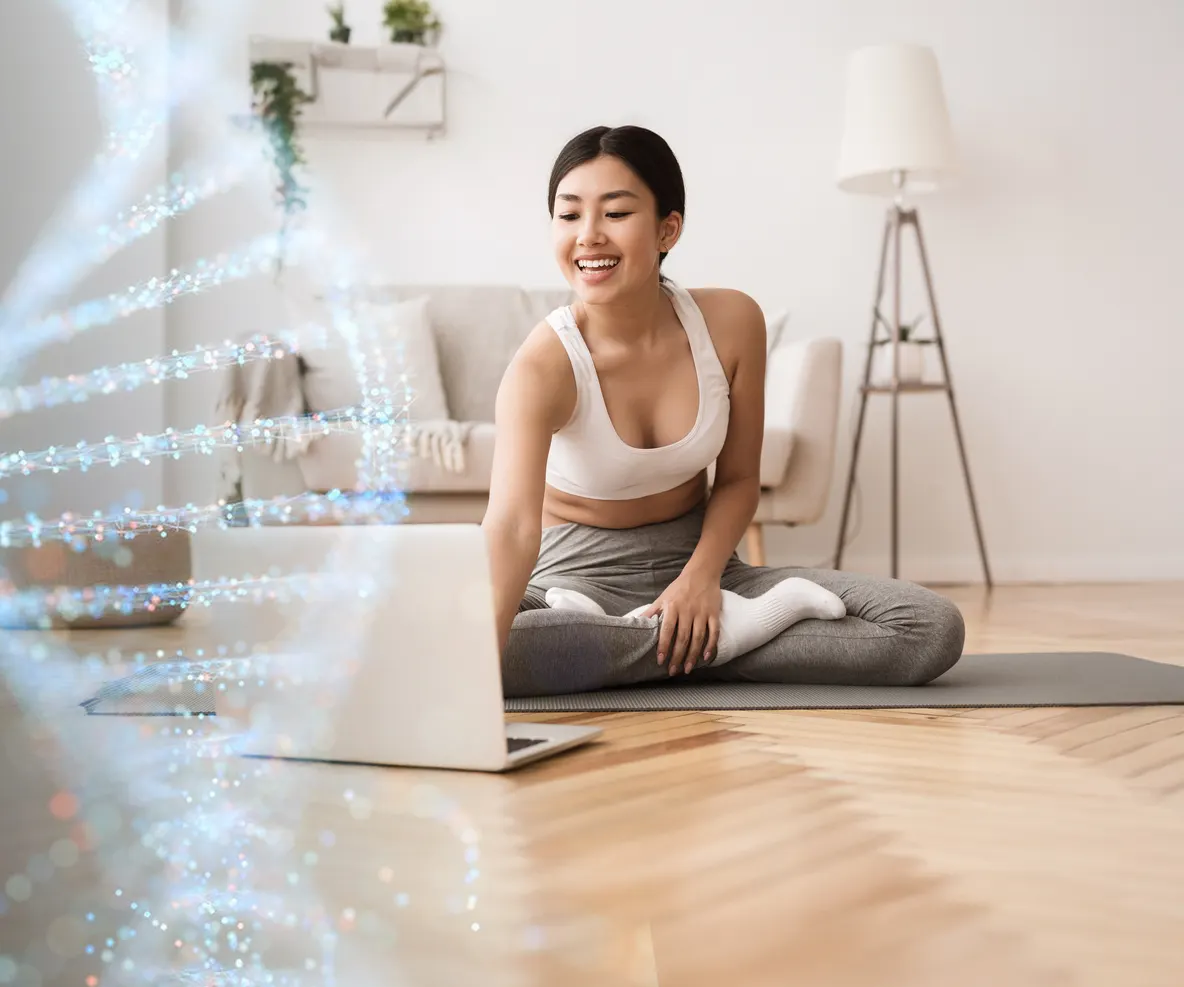 A woman sitting on a yoga mat at home, smiling at a laptop, with a DNA strand drawn over the left of the picture