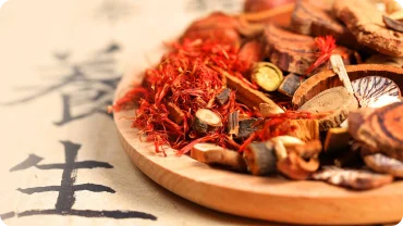 Dried herbs on a wooden dish beside Chinese calligraphy